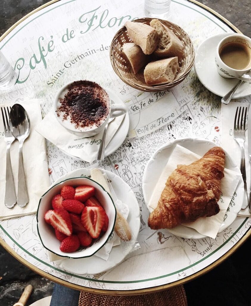 A breakfast table at Café de Flore in Paris, featuring a croissant, strawberries, coffee, and hot chocolate.